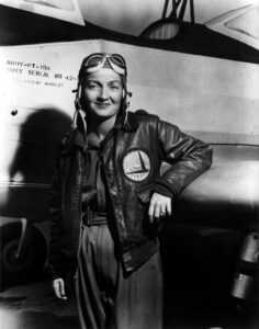 A black and white photo of a Woman Airforce Service Pilot standing in front of a military aircraft from World War II.